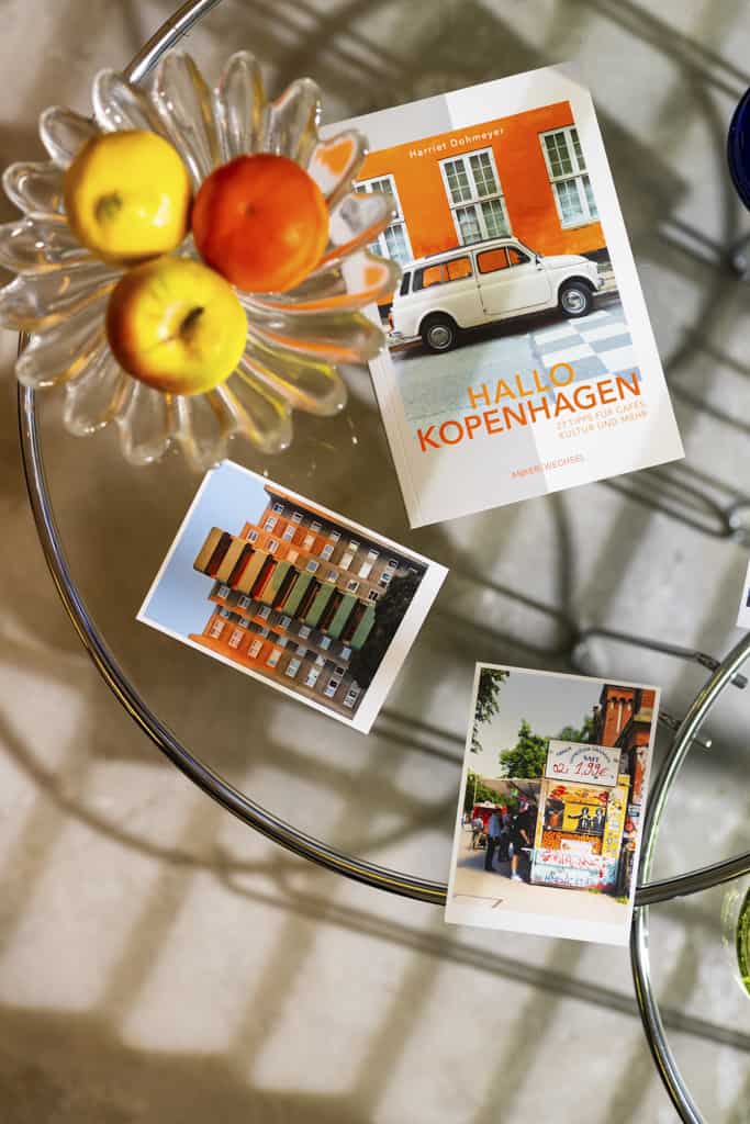 "Hallo Kopenhagen" – Ankerwechsel Verlag Buch im Studio von Ain't No Trash auf Glastisch mit Postkarten und Obstschale
