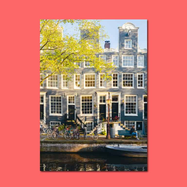 Fotodruck einer Amsterdamer Gracht mit Giebelhäusern und Booten im Herbstlicht