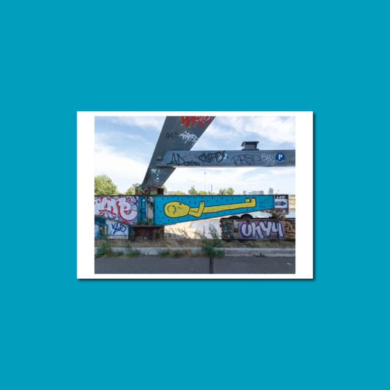 Postkarte mit Graffiti in Amsterdam-Noord: liegende gelbe Figur auf blauer Wand unter einer Brücke