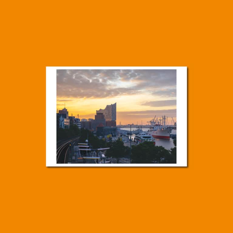 Postkarte mit Blick über den Hamburger Hafen: Elbphilharmonie und Schiffe im Sonnenaufgang, Hochbahngleise im Vordergrund