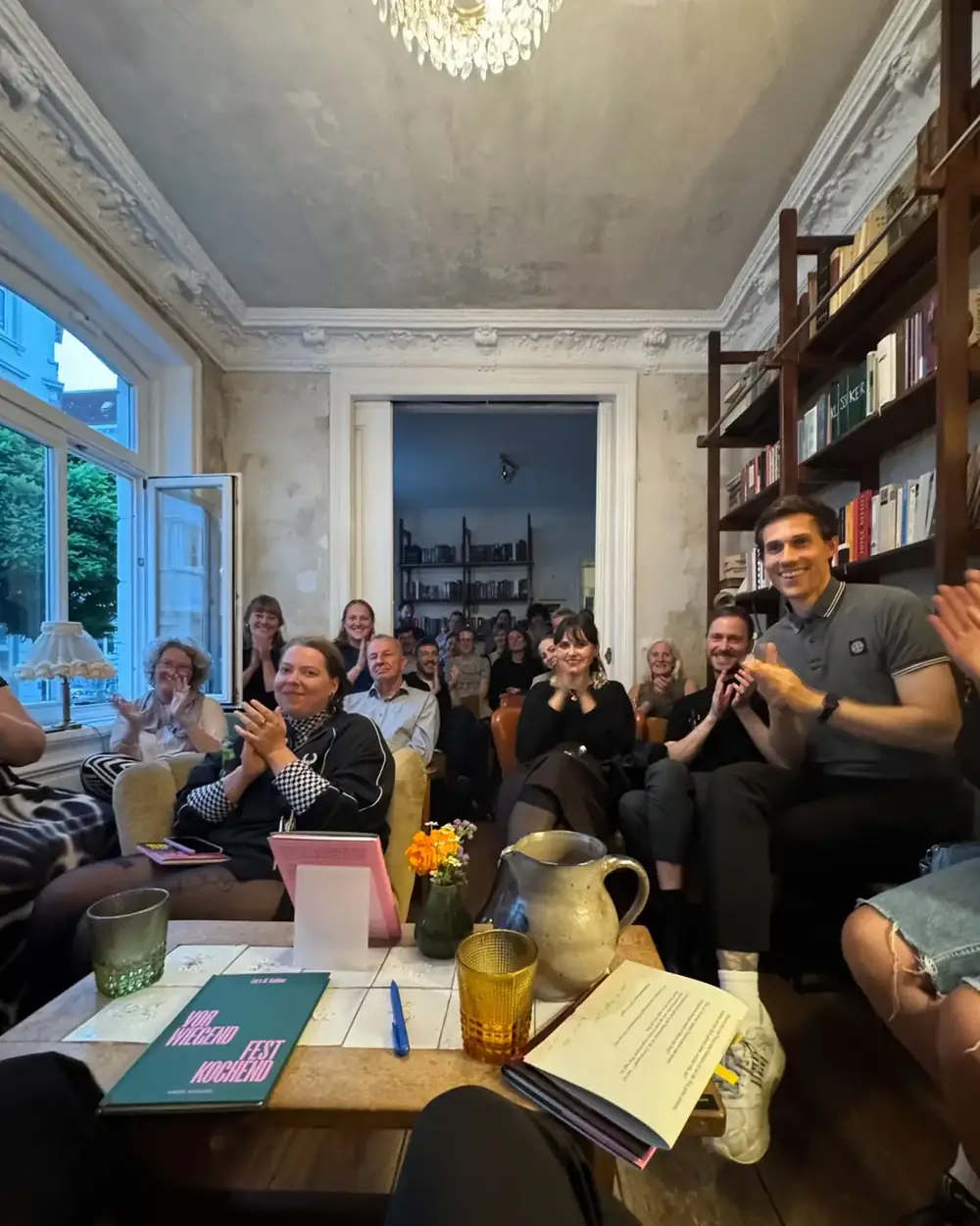 Ein voller Raum mit Sesseln und Bücherregalen, das Publikum applaudiert, auf dem Tisch liegt das Buch „Vorwiegend festkochend“