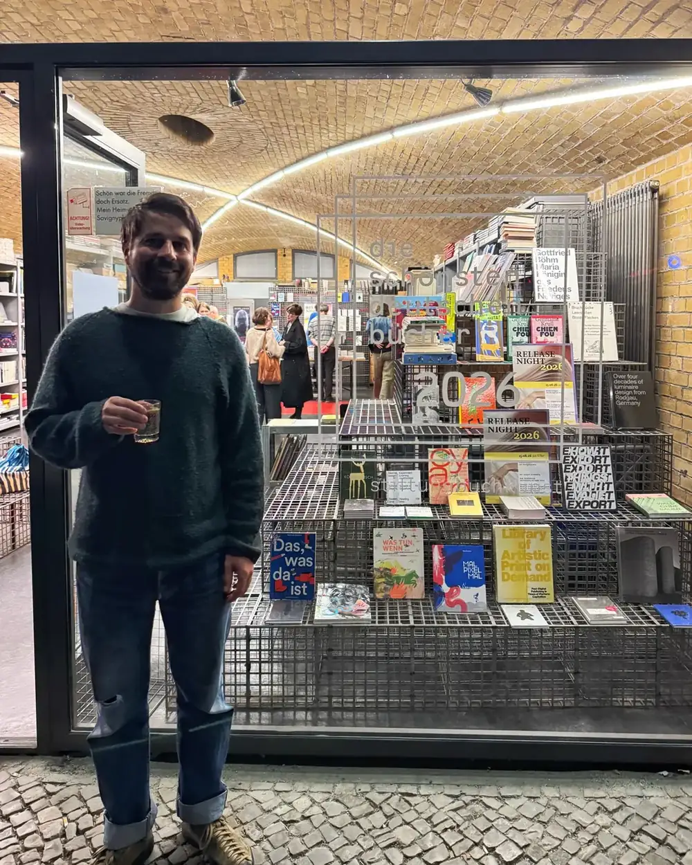 Ein Schaufenster mit den ausgezeichneten Büchern des Jahrgangs, davor steht Konrad Staisch mit einem Glas in der Hand