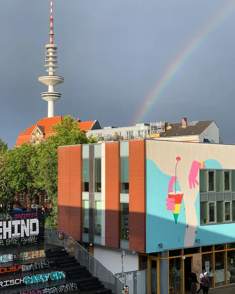 Blick über St. Pauli: der Hamburger Fernsehturm, ein Regenbogen und das Gebäude mit dem Musikclub, an der Fassade ein großes Wandbild