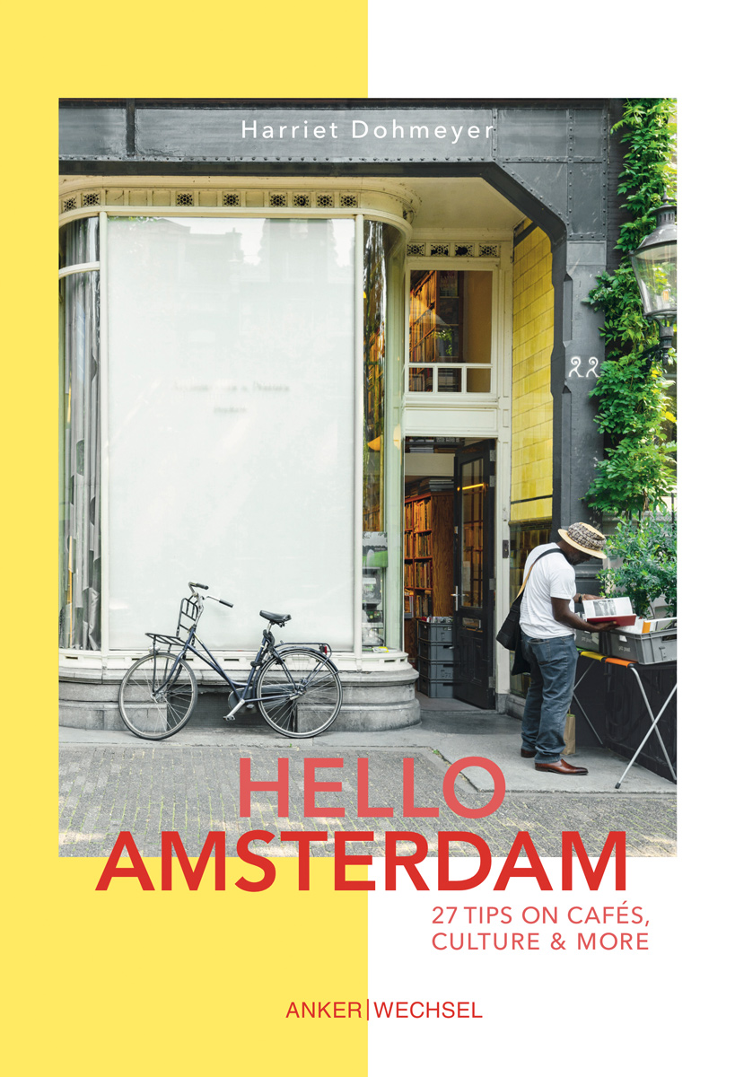 Buchcover Hello Amsterdam: Amsterdamer Ladenfront mit abgestelltem Fahrrad, davor blättert eine Person in einem Buch