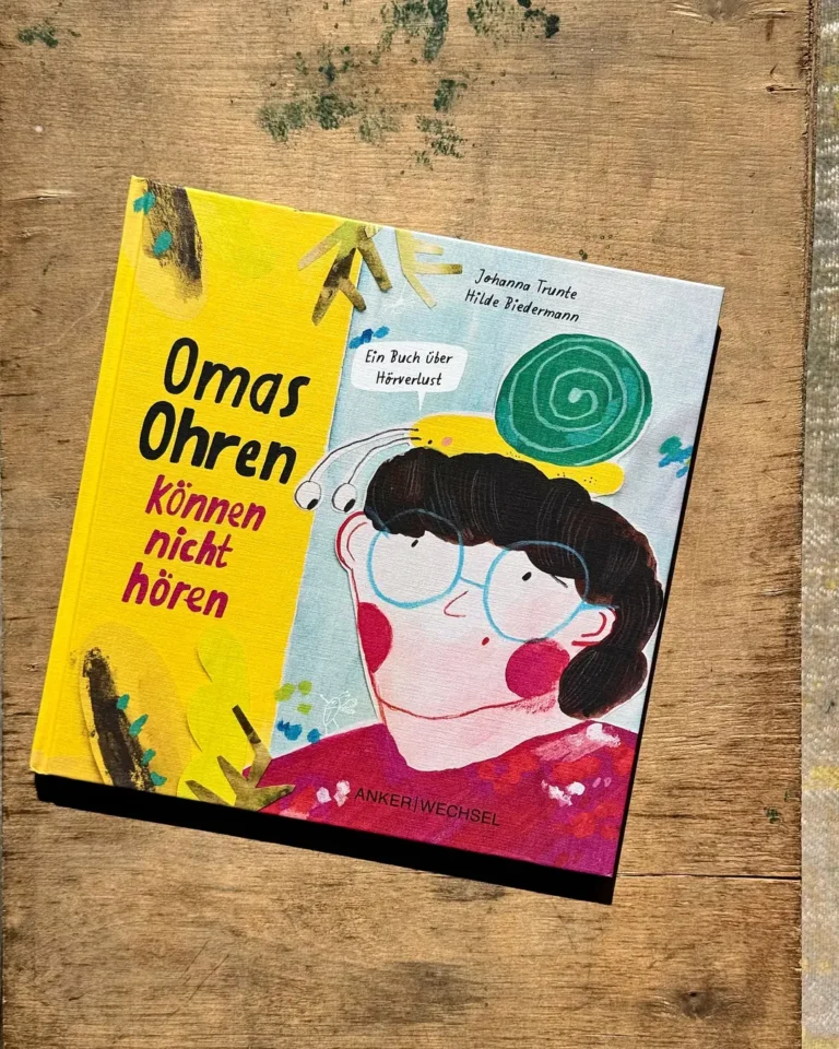 Das gedruckte Bilderbuch „Omas Ohren können nicht hören“ liegt in der Sonne auf einem alten Holztisch